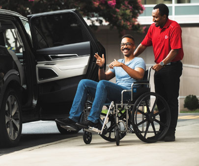 Employé SP+ poussant une personne en fauteuil roulant jusqu'à sa voiture